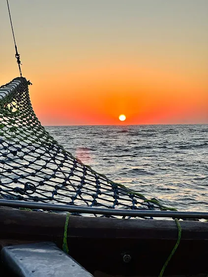 Pôr do sol laranja no horizonte do mar, visto da rede na proa do barco
