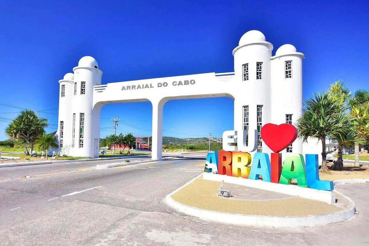 Pórtico branco de entrada de Arraial do Cabo, com o letreiro colorido Eu amo Arraial sob céu azul